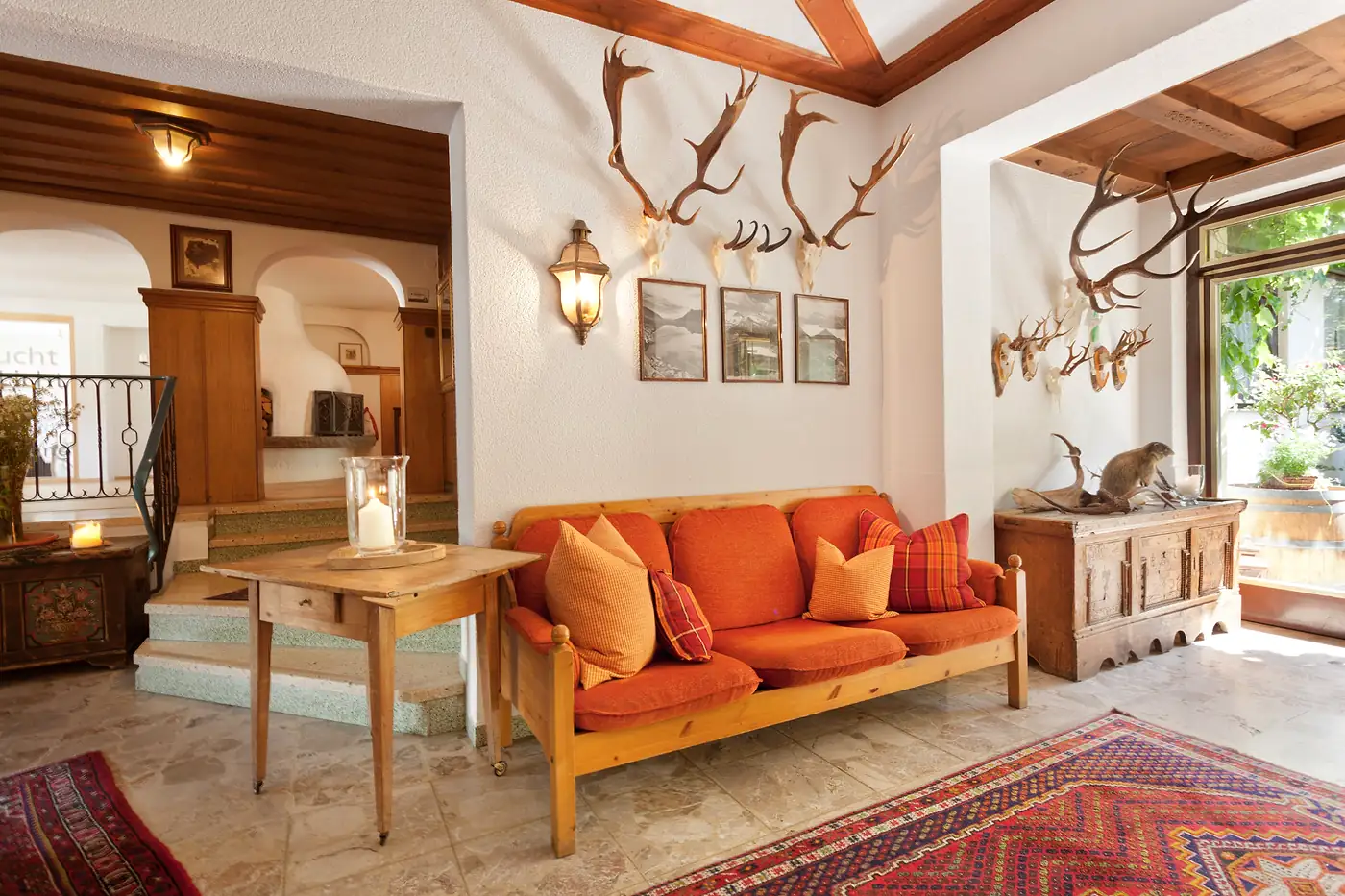 Empfangsraum mit Geweihen an der Wand, orangem Sofa und Teppichen