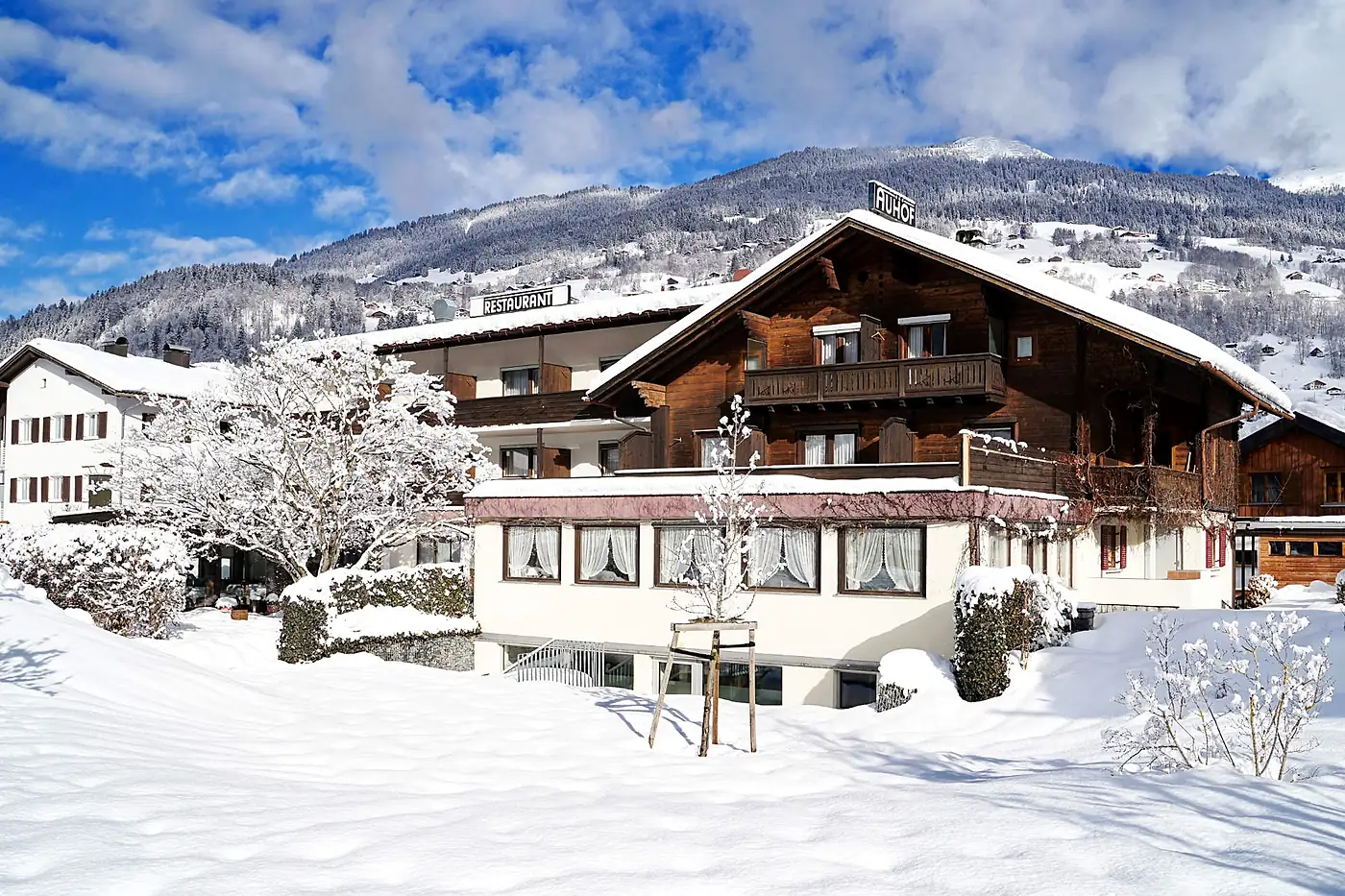 Der Auhof im Winter: Holzhaus mit Balkon unter Schnee vor dem Berghang